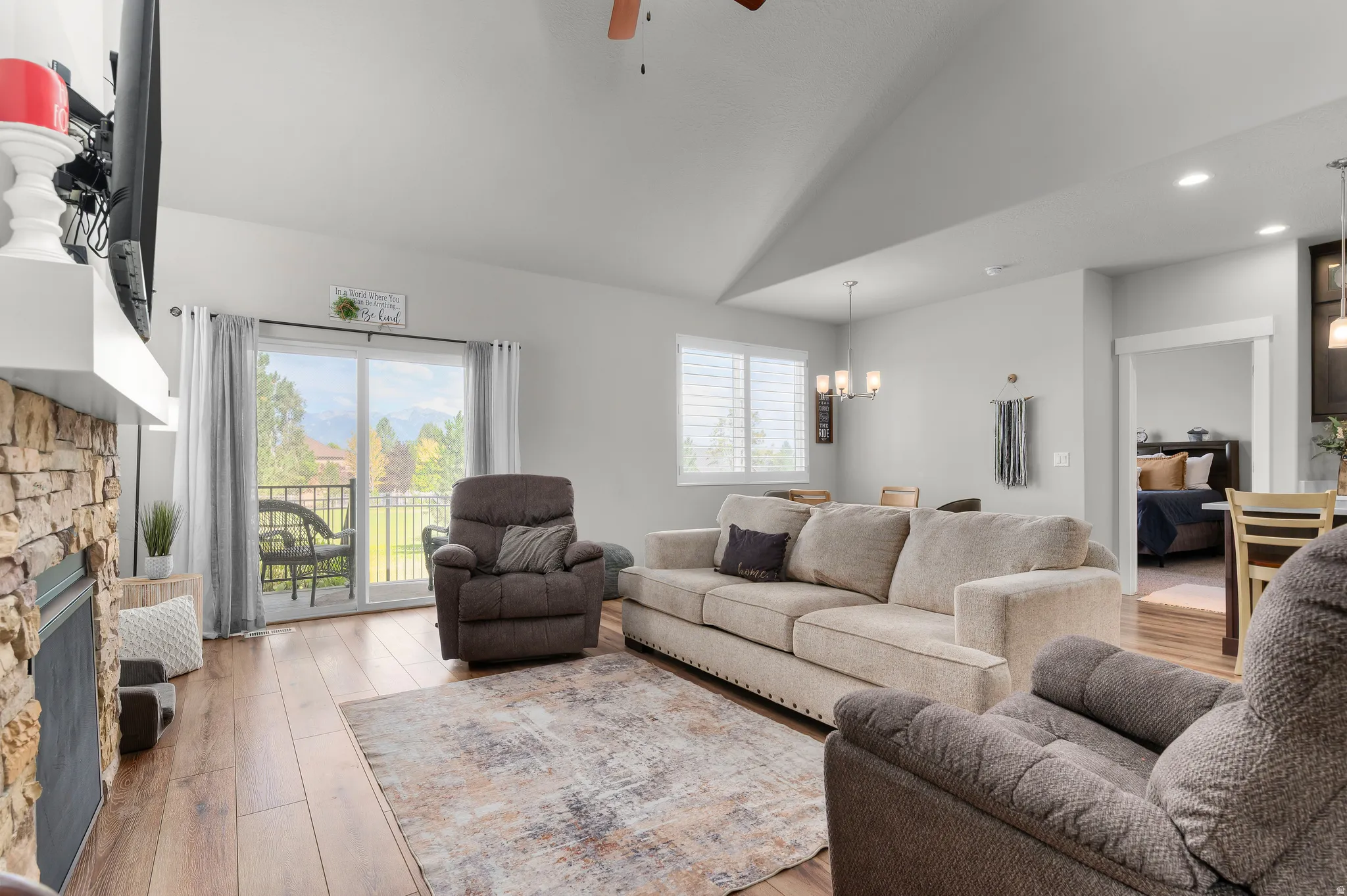 Spacious living area featuring vaulted ceilings, wood-finish flooring, and a stacked stone fireplace with a white mantel