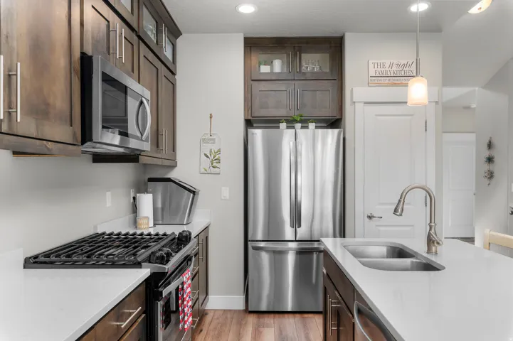 Kitchen featuring stainless steel appliances, dark wood-finish cabinetry, light countertops, a gas range, and a double basin sink with a brushed nickel faucet