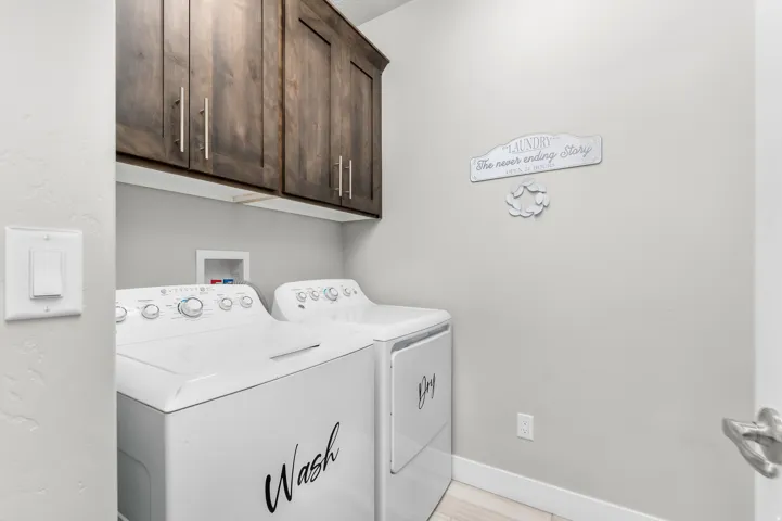 Dedicated laundry area featuring dark wood-finish cabinetry with brushed nickel hardware, white appliances, and light wood-finish flooring
