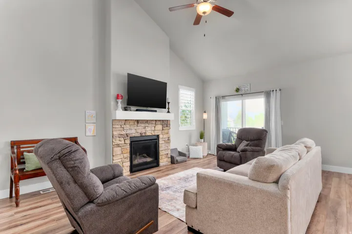 Vaulted ceilings enhance this living space, featuring wood-finish flooring and a stone-clad fireplace with a white mantel