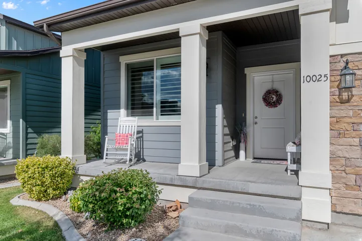 Covered front porch featuring a white entry door, stone veneer accents, gray siding, and a prominent address number