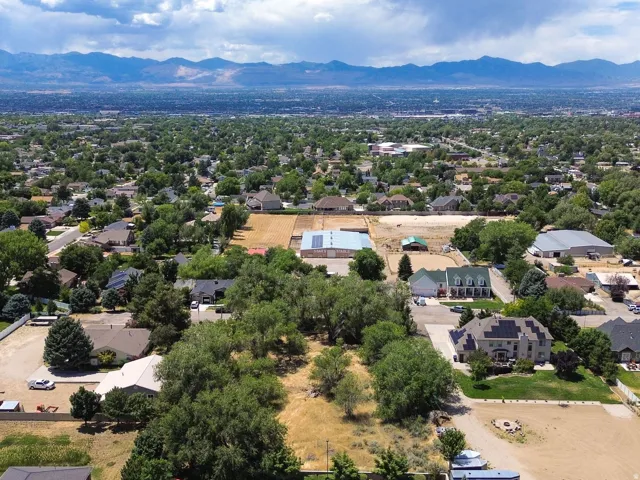 Expansive parcel featuring mature trees, surrounding residential homes, open land, and distant mountain ranges