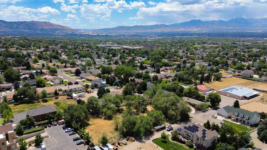Expansive aerial view of a residential area featuring a variety of housing styles, mature trees, and mountainous terrain in the distance