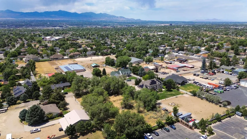 Expansive aerial view showcasing a mixed-use neighborhood with residential properties, commercial structures, and undeveloped land parcels
