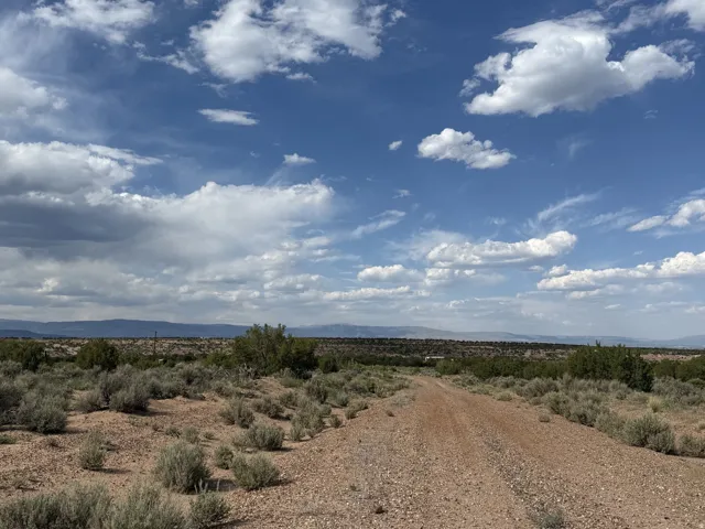 Expansive raw land featuring a gravel road, distant mountain ranges, and natural shrubbery under a clear sky