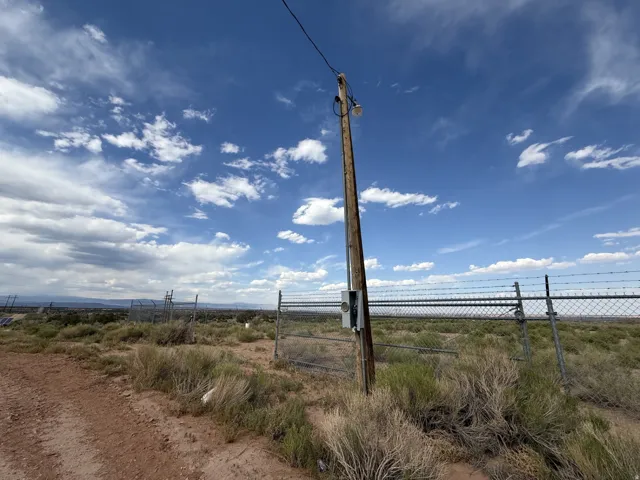 Property featuring a wooden utility pole with an attached old electrical box, chain-link fencing with barbed wire, arid landscaping, and a clear expanse of sky