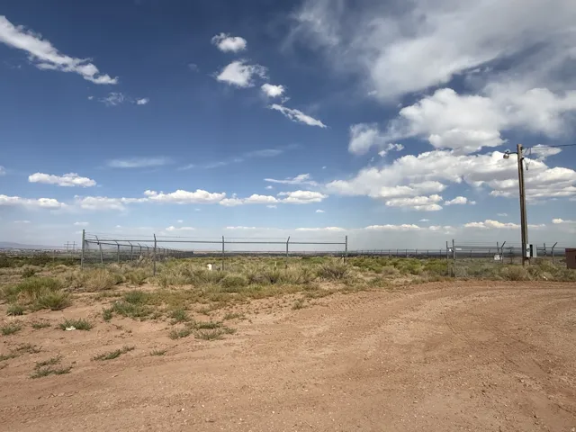 Expansive open land with a chain-link perimeter fence, a dirt road, and scattered scrub brush