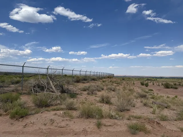 Extensive parcel featuring a chain-link fence with barbed wire, desert vegetation, and open land