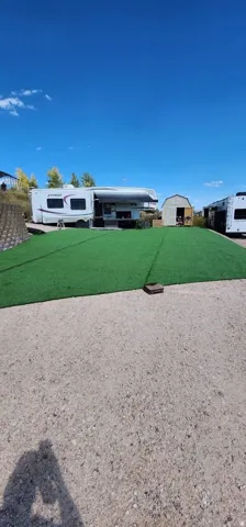 Gravel lot featuring an artificial turf area with a visible storage shed