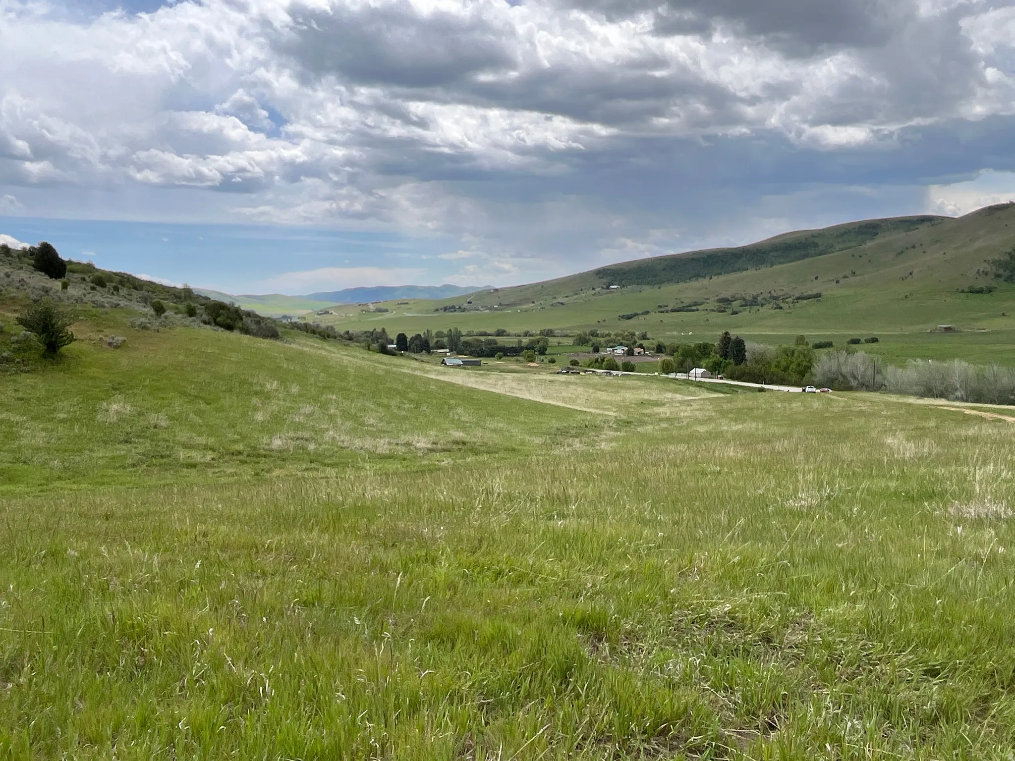 Expansive green terrain with rolling hills and a distant valley, featuring scattered trees and a visible road