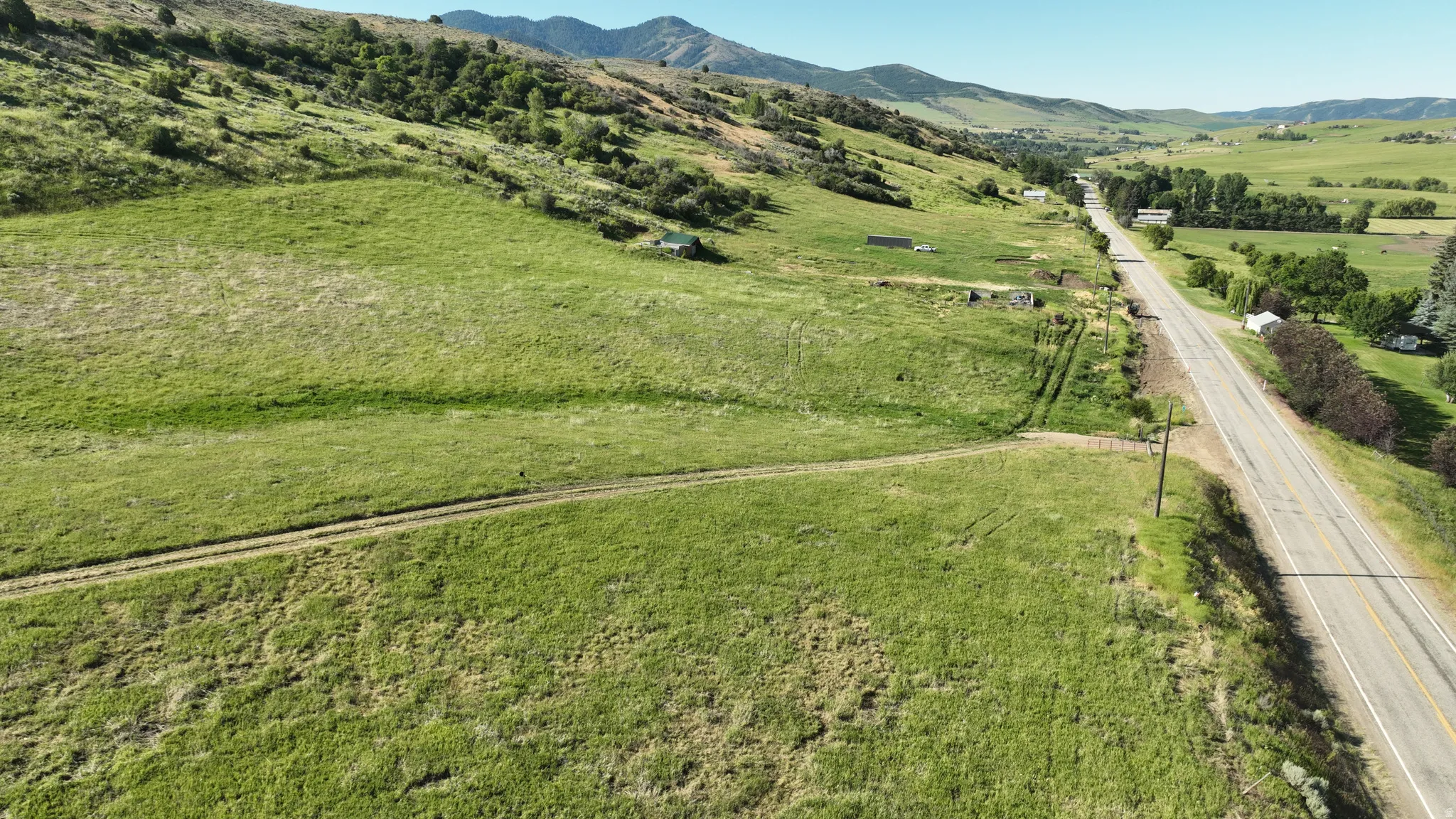 Expansive green acreage featuring a winding dirt path, distant mountain backdrop, and a paved two-lane road