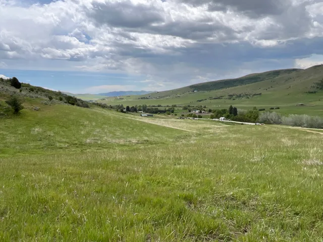 Expansive green terrain with rolling hills and a distant valley, featuring scattered trees and a visible road