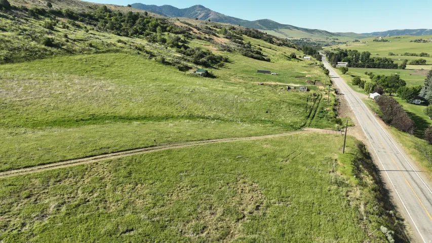 Expansive green acreage featuring a winding dirt path, distant mountain backdrop, and a paved two-lane road