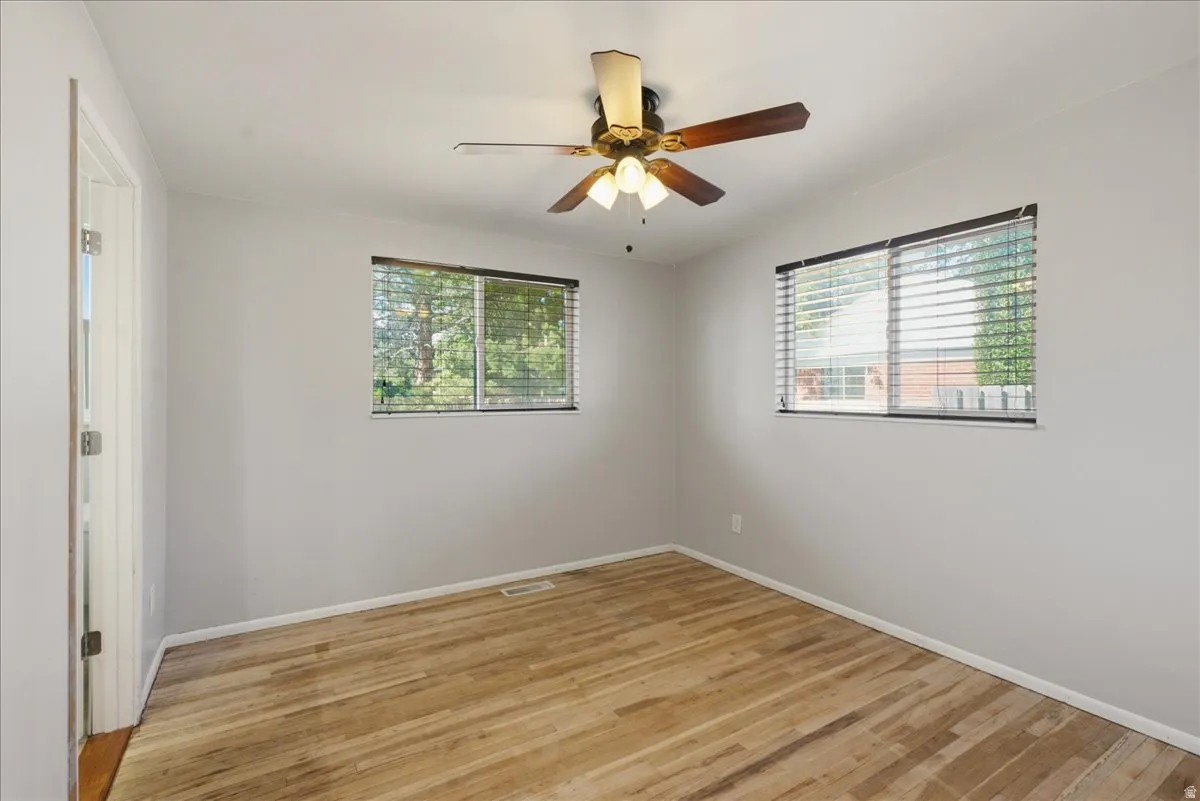 Light gray walls, wood-finish flooring, and a ceiling fan with light fixture