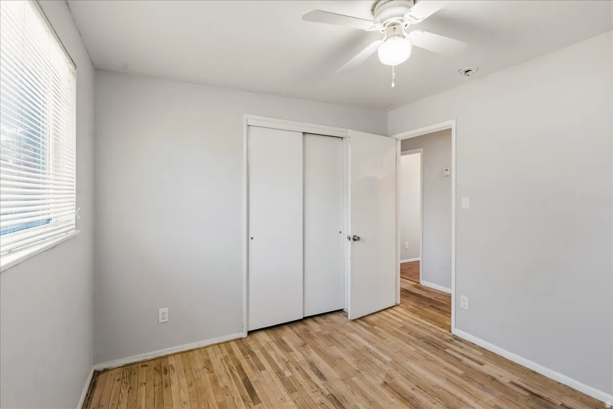 Room featuring wood-finish flooring, a window with horizontal blinds, and a ceiling fan with integrated lighting