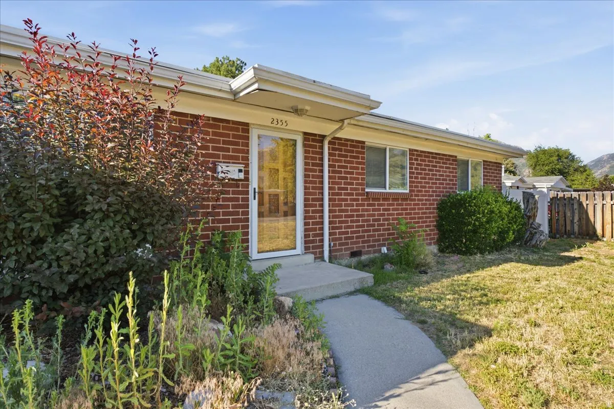 Brick exterior featuring a concrete walkway, established shrubbery, and a front entry door with a glass panel