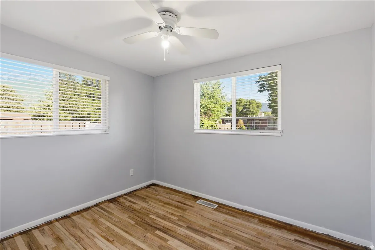 Room featuring two windows with horizontal blinds, wood-finish flooring, and light gray wall paint