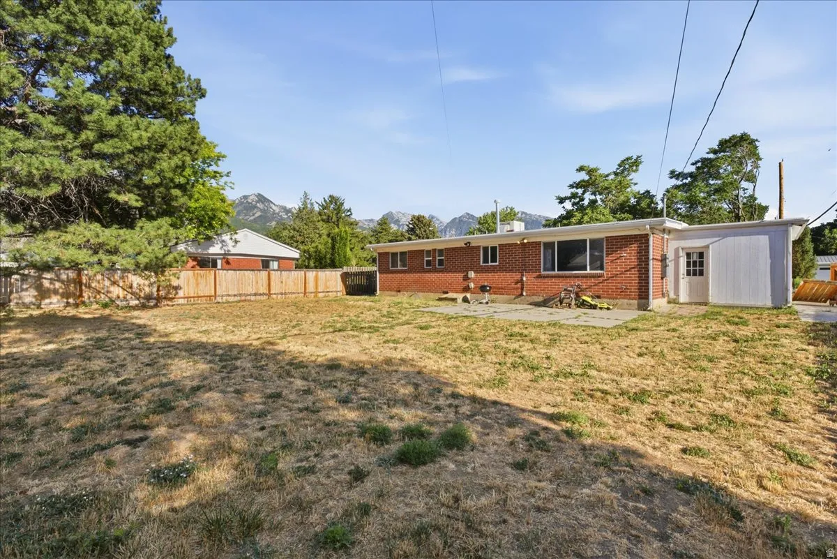 Spacious backyard with a wooden privacy fence, mature trees, mountain backdrop, red brick exterior, and a concrete patio area