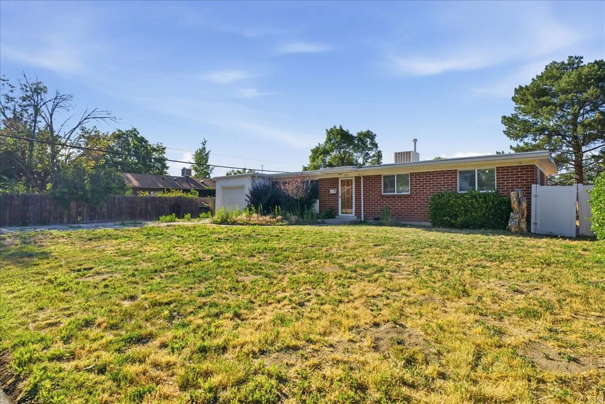 Brick ranch-style home featuring a front yard, attached garage, and mature landscaping