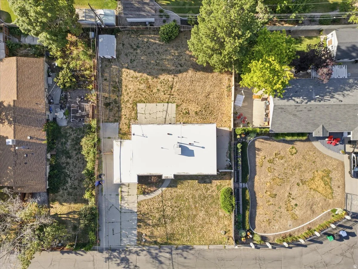 Expansive lot featuring a single-story residence with a white flat roof, concrete driveway, and surrounding undeveloped land