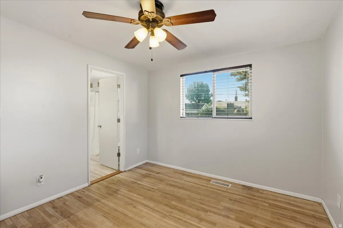 Room featuring light wood-finish flooring, a ceiling fan with light fixture, and a window with horizontal blinds