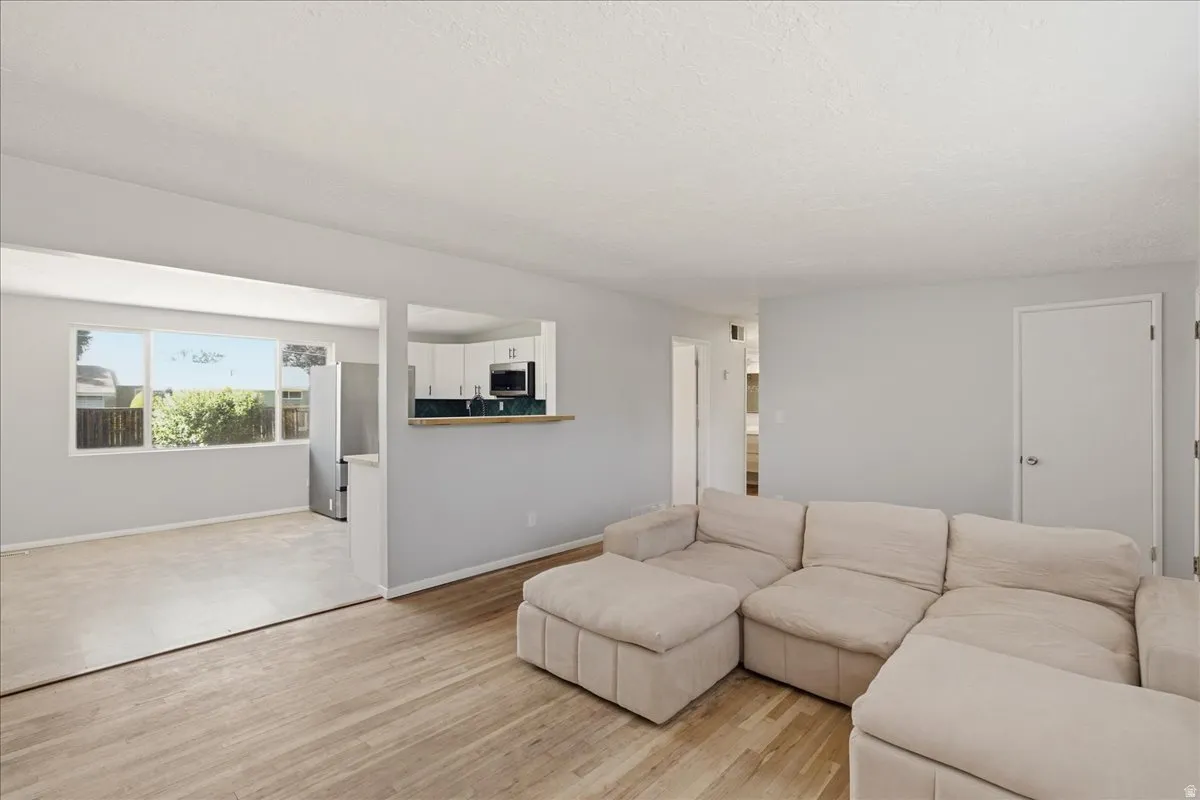 Bright living area featuring light wood-finish flooring, a pass-through window to the kitchen, and a large picture window