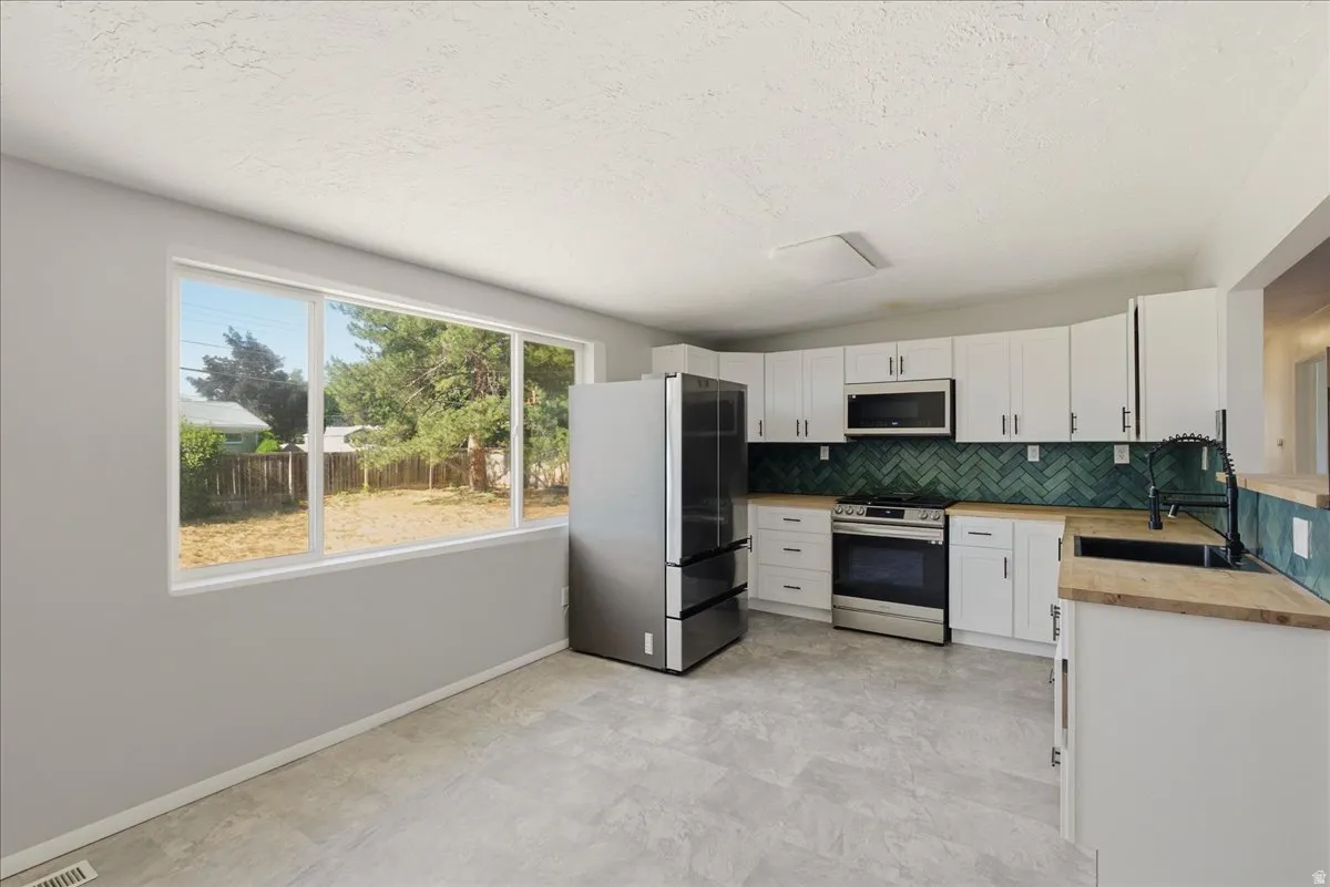 Kitchen featuring white cabinetry, light wood-finish countertops, and a green herringbone tile backsplash
