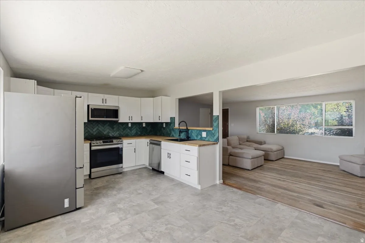 Modern kitchen featuring white cabinetry, stainless steel appliances, butcher block style countertops, and a teal herringbone tile backsplash