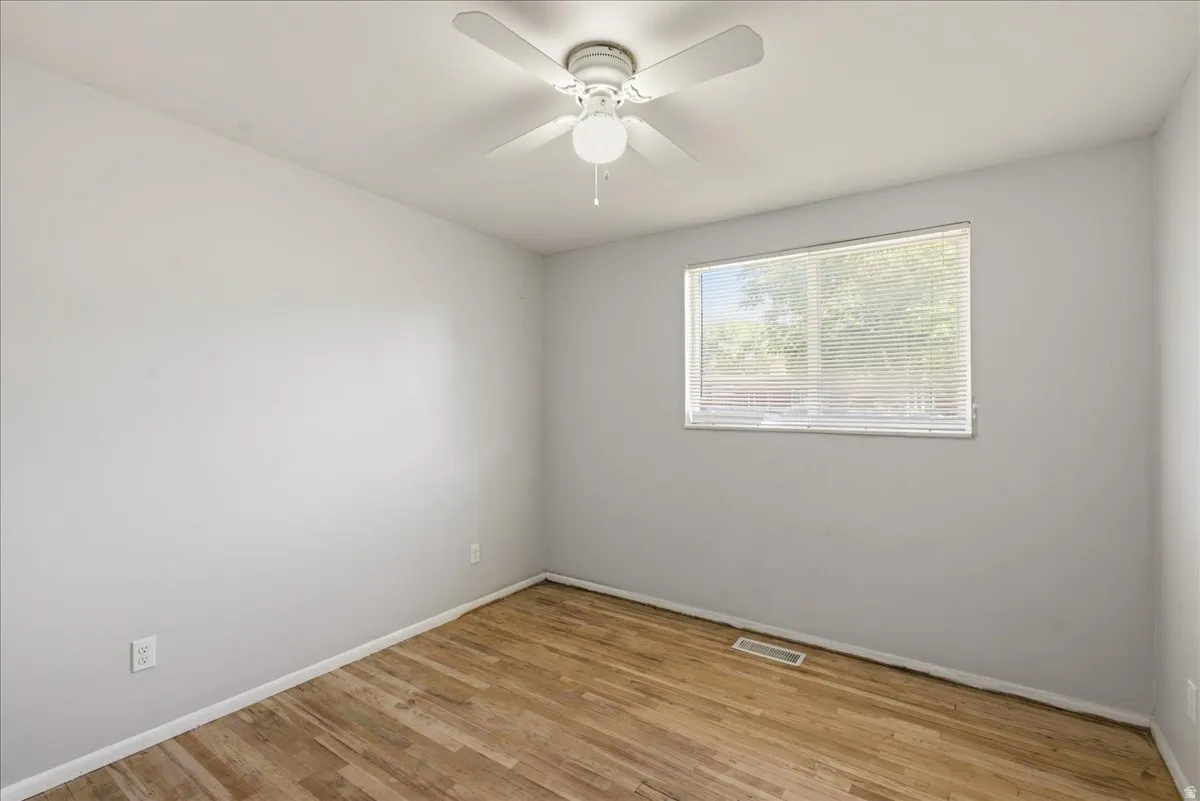 Room featuring wood-finish flooring, a white ceiling fan with integrated lighting, a rectangular window with horizontal blinds, and light-toned walls