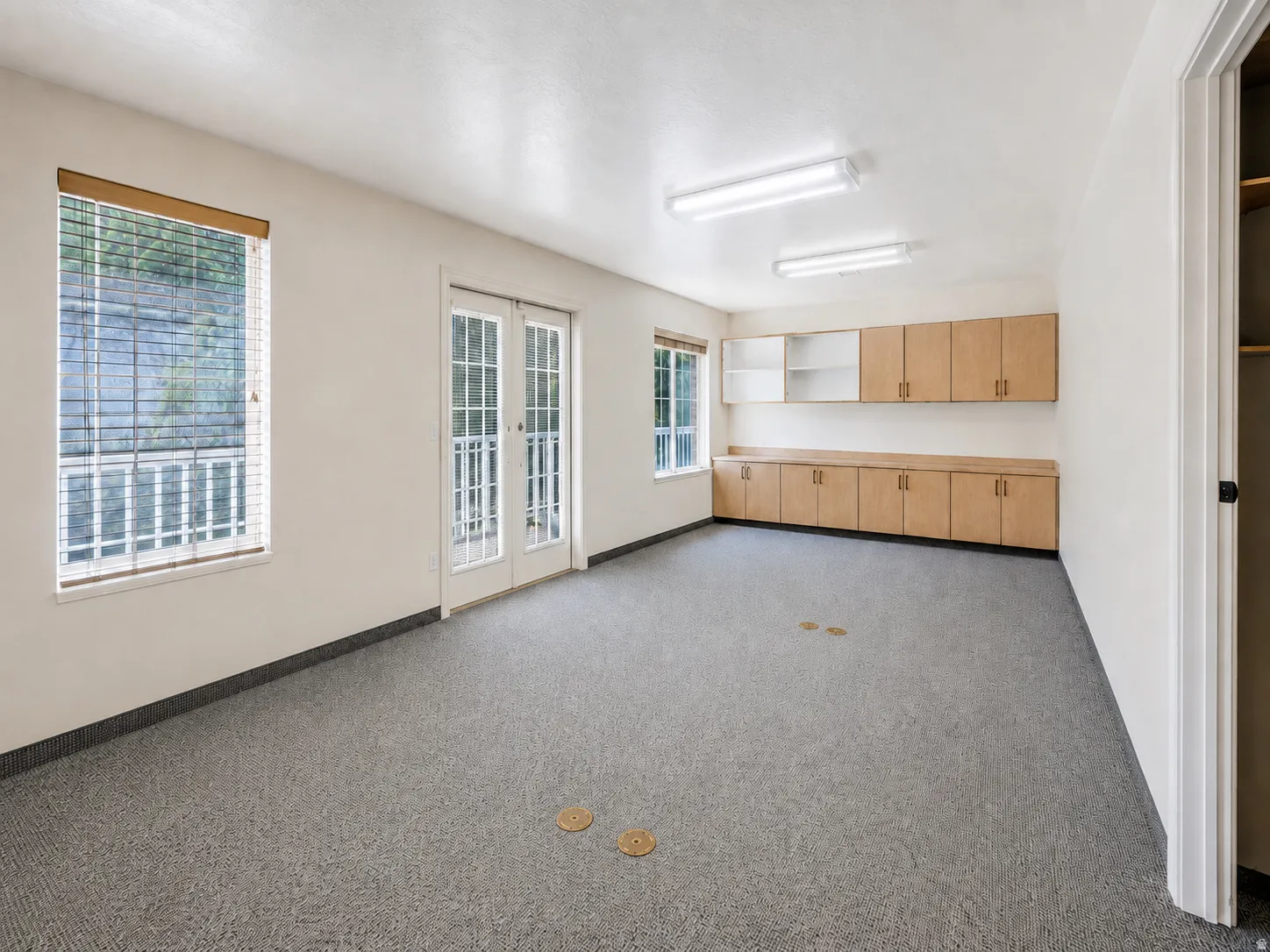 Spacious room featuring light-colored walls, durable grey flooring, and ample natural light from two windows and French doors