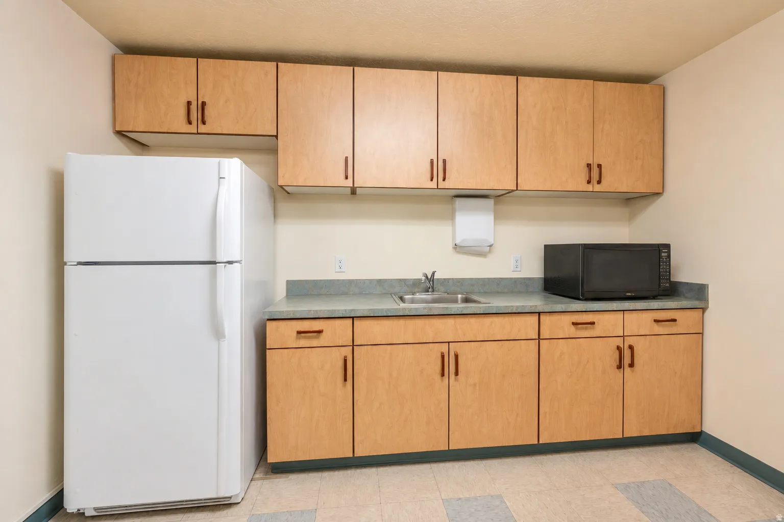 Kitchenette featuring extensive wood-finish cabinetry, a built-in stainless steel sink, and durable laminate countertops