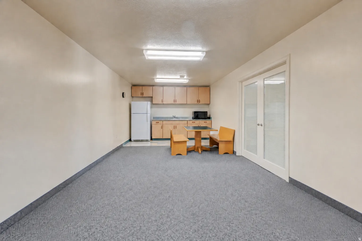 Open-plan area featuring light-toned walls, gray patterned carpeting, and white baseboards