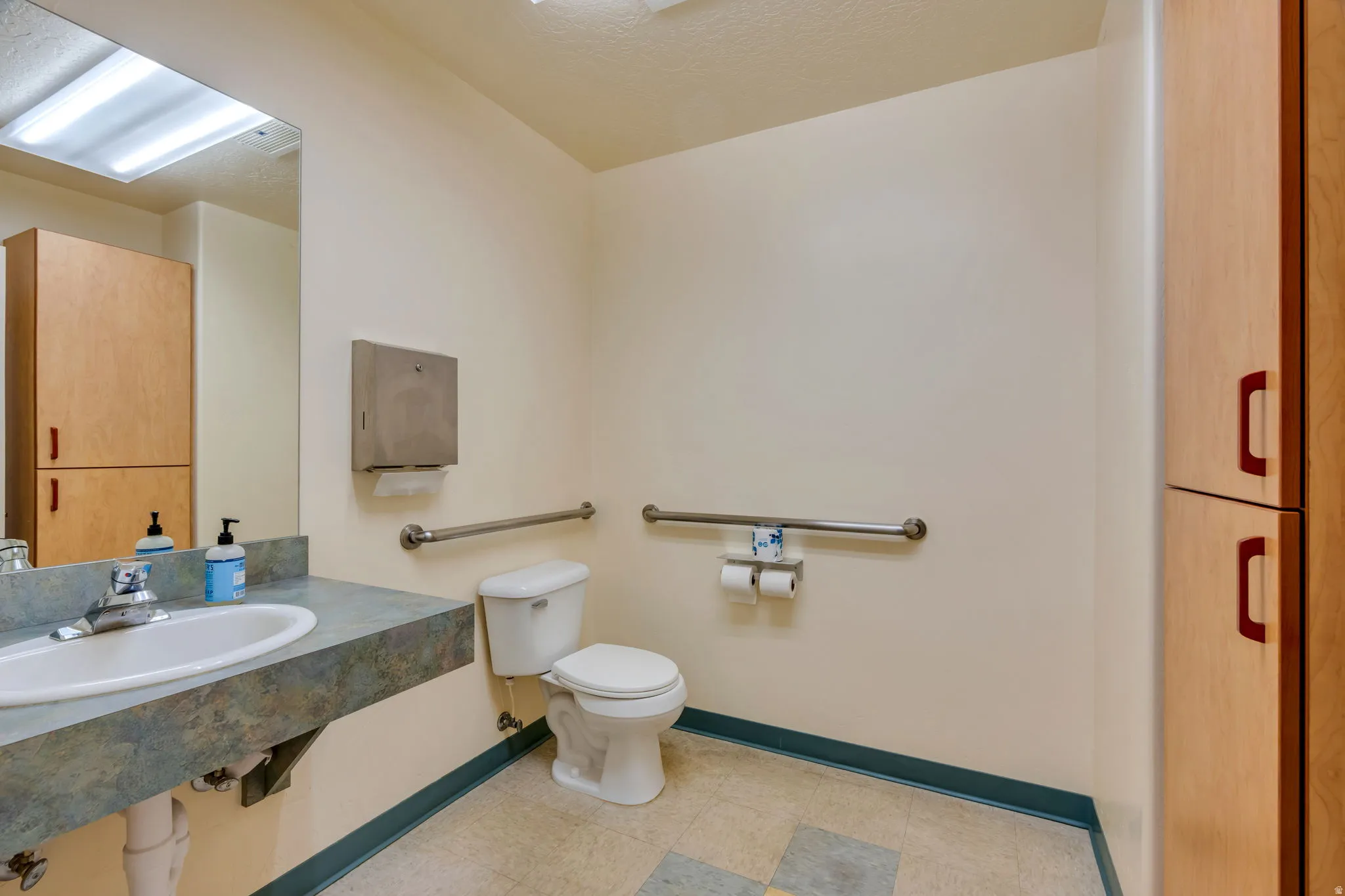 Bathroom featuring a rectangular sink set in a speckled countertop, a toilet, and two sets of horizontal grab bars