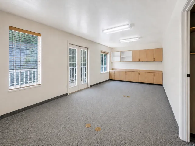 Spacious room featuring light-colored walls, durable grey flooring, and ample natural light from two windows and French doors