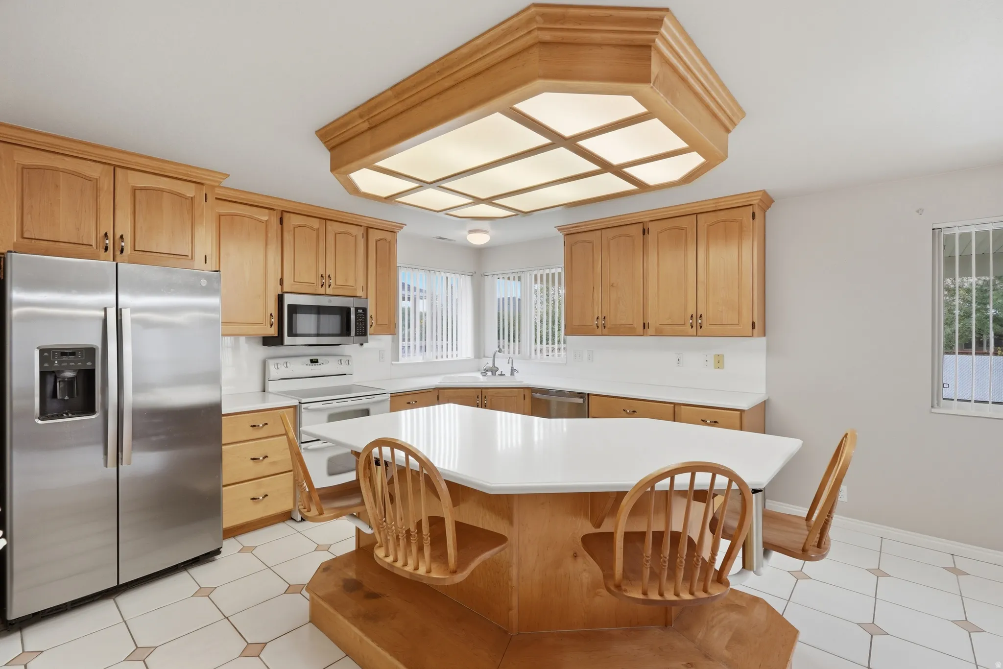 Kitchen with light wood cabinetry, stainless steel appliances, and a built-in island with a white countertop