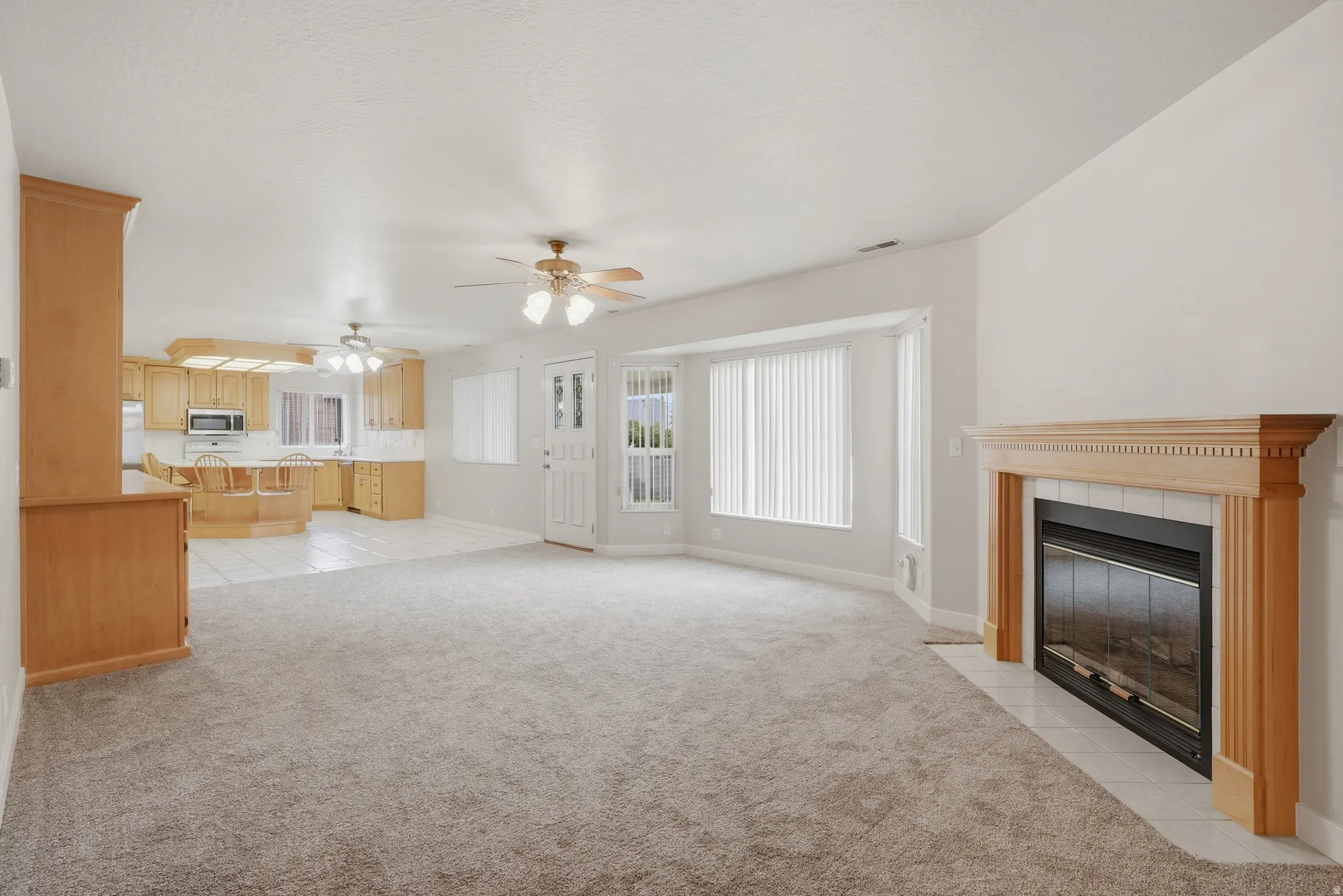 Open-concept living space featuring a fireplace with a wood mantle, bay windows, and carpeted flooring