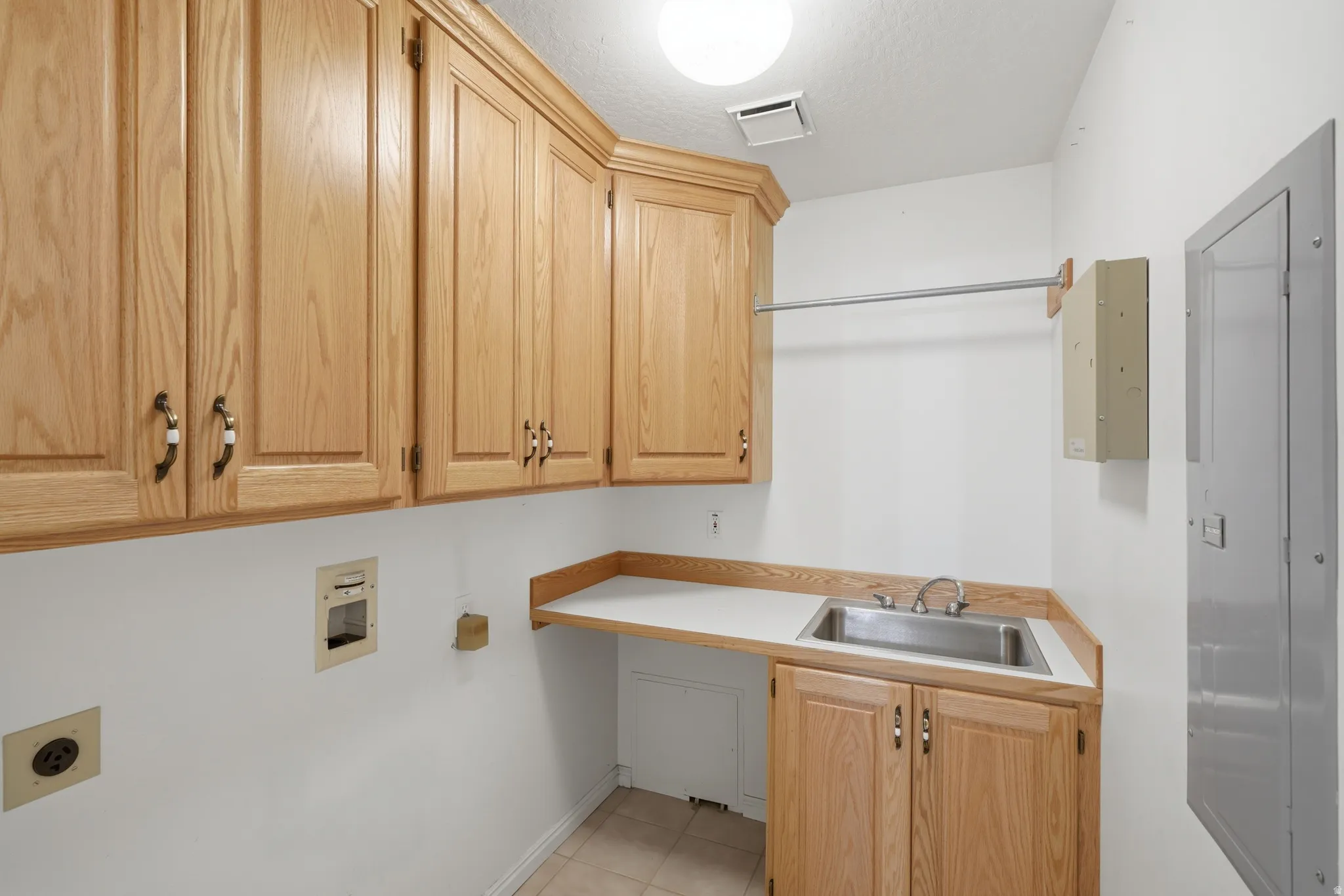 Utility room featuring extensive wood cabinetry, a stainless steel sink, and a built-in hanging rod