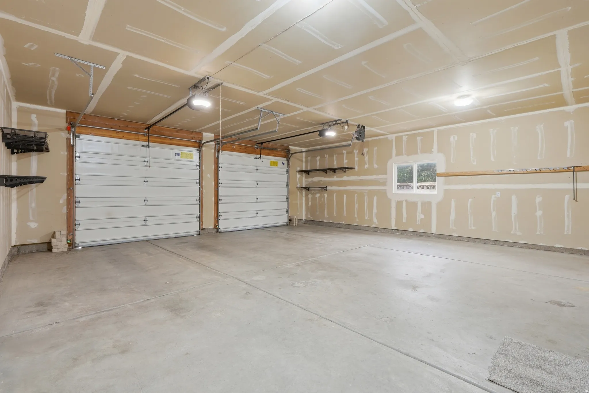 Spacious two-car garage featuring a concrete floor, two individual garage doors with openers, built-in shelving, and a window for natural light