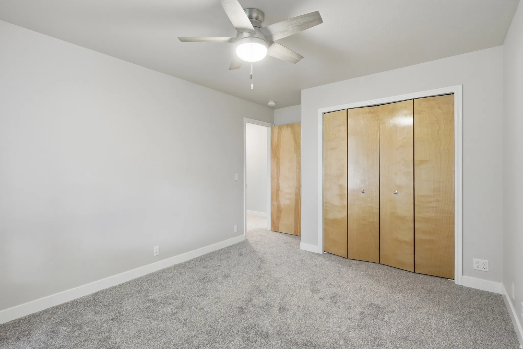 Neutral-toned room featuring a ceiling fan with light fixture, light gray walls, and gray carpet