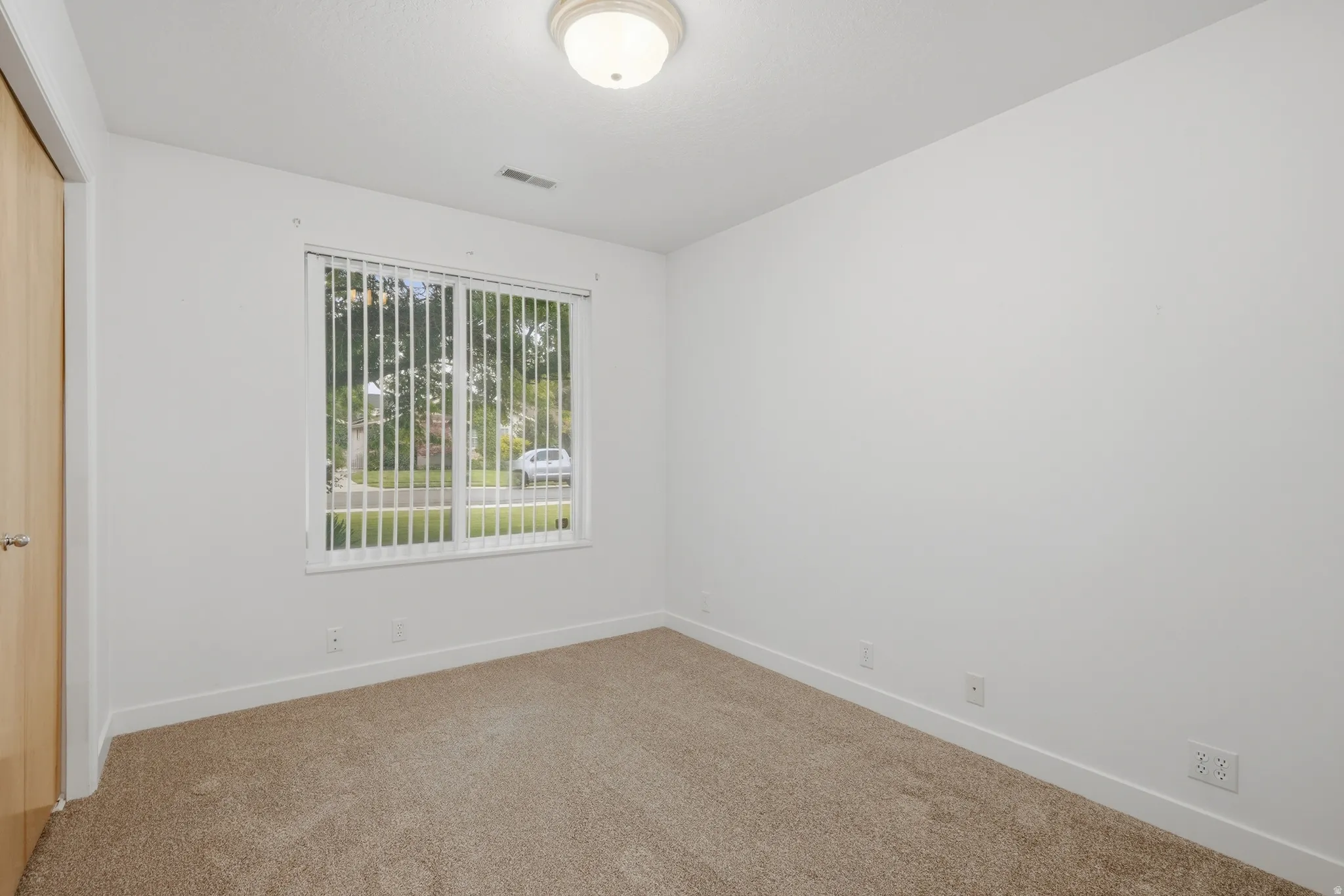 Interior room featuring neutral carpeting, white walls, and a large window with vertical blinds