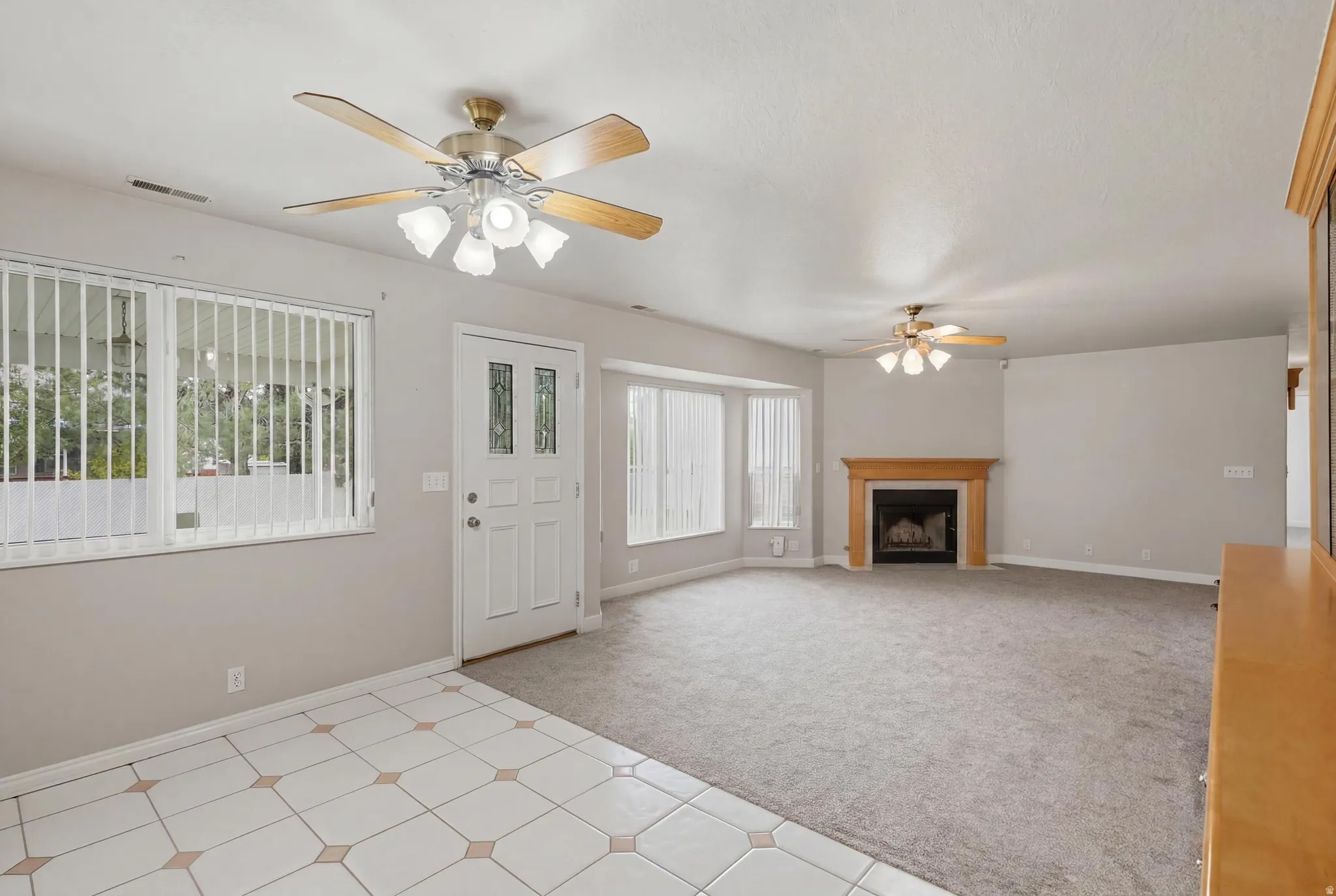 Spacious interior featuring a fireplace with a wood mantel, multiple ceiling fans, and a combination of tiled and carpeted flooring