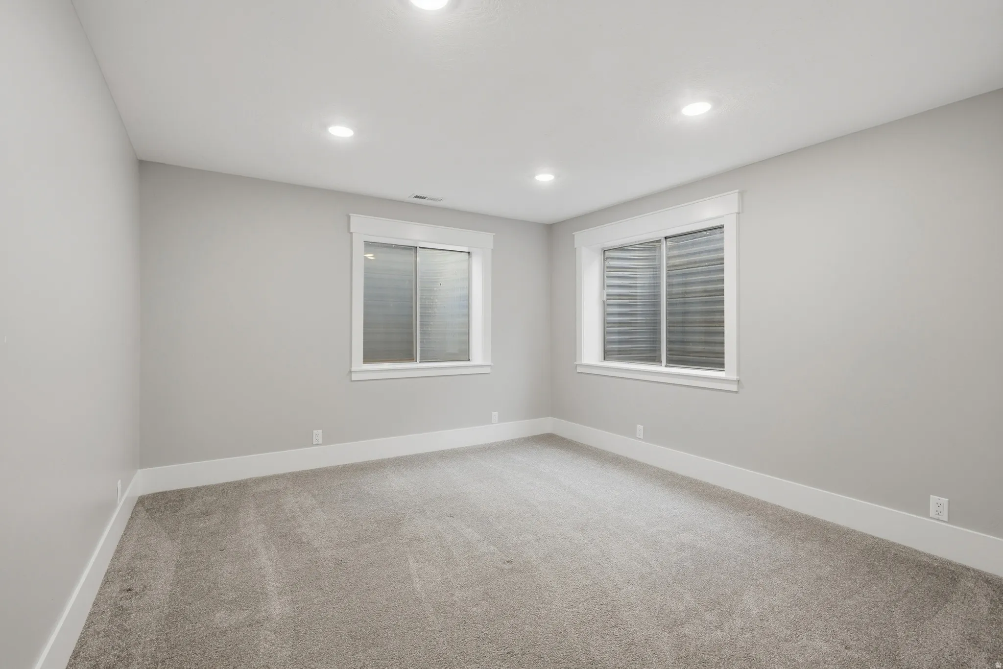 Spacious room with light gray walls, plush gray carpeting, and two egress windows with white trim