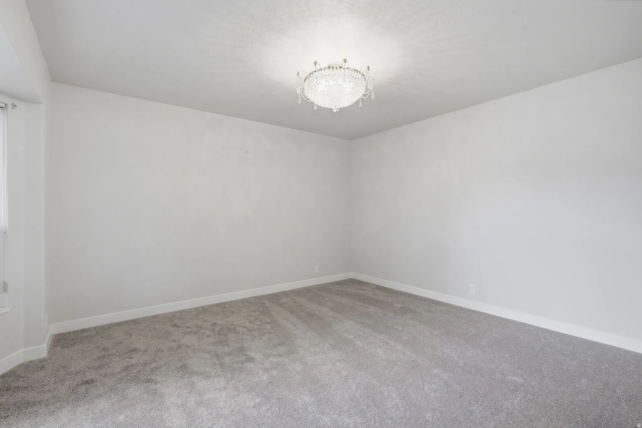 Spacious room featuring a crystal chandelier, neutral wall paint, gray carpeting, and white baseboards