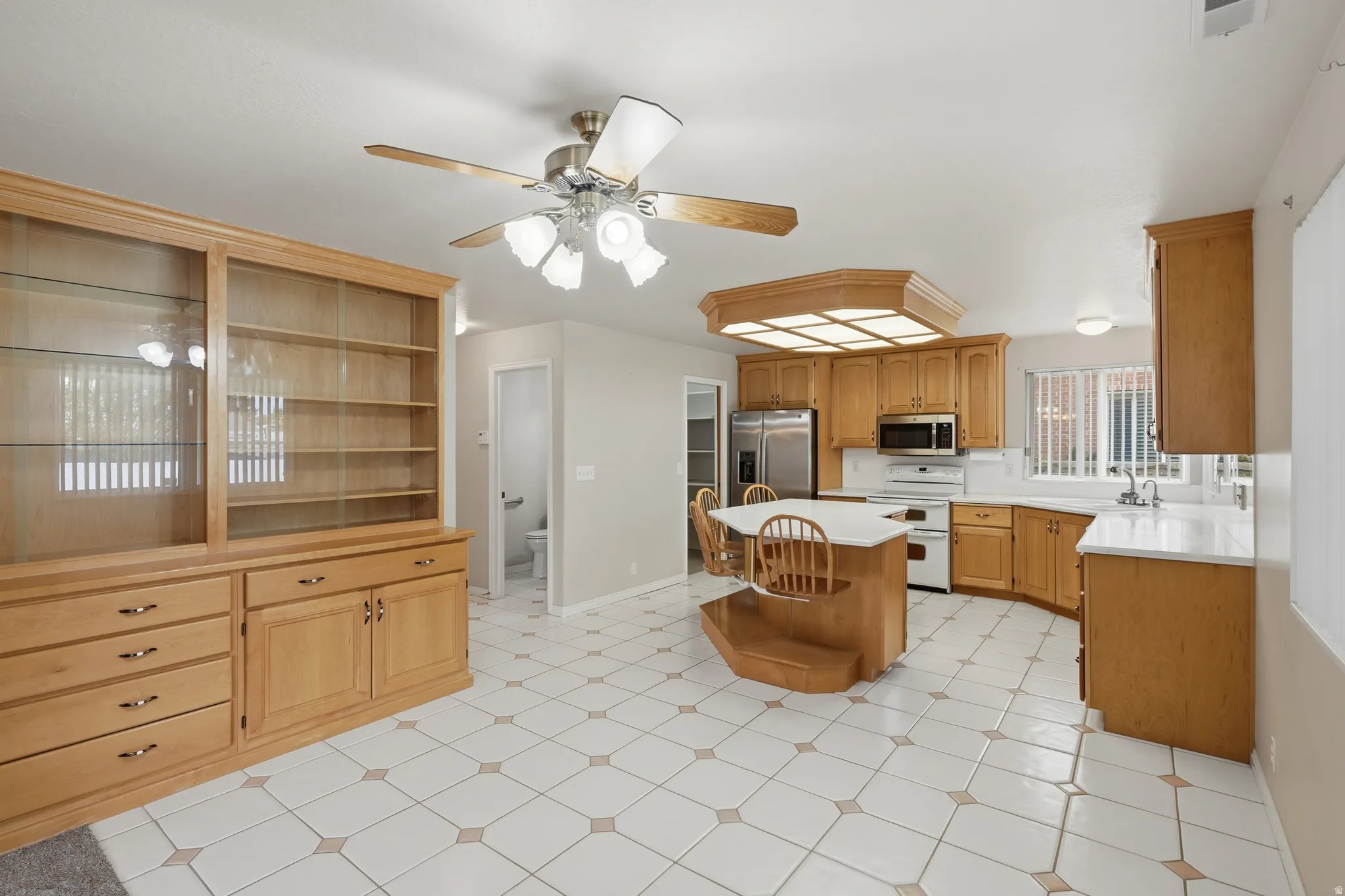 Open-concept kitchen and living area featuring tile flooring, light wood cabinetry, white countertops, and a central island with seating