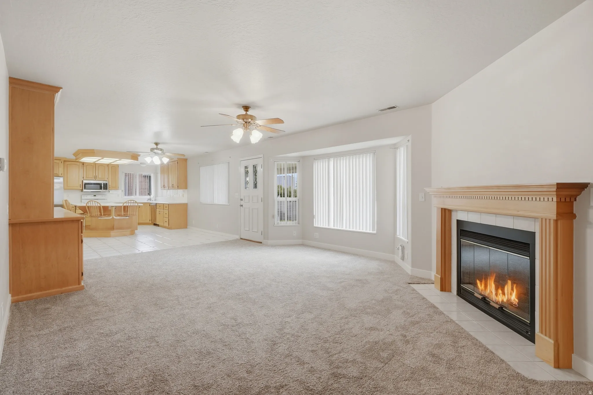 Spacious living area featuring a fireplace with a light wood mantel, neutral carpet flooring, and a bay window