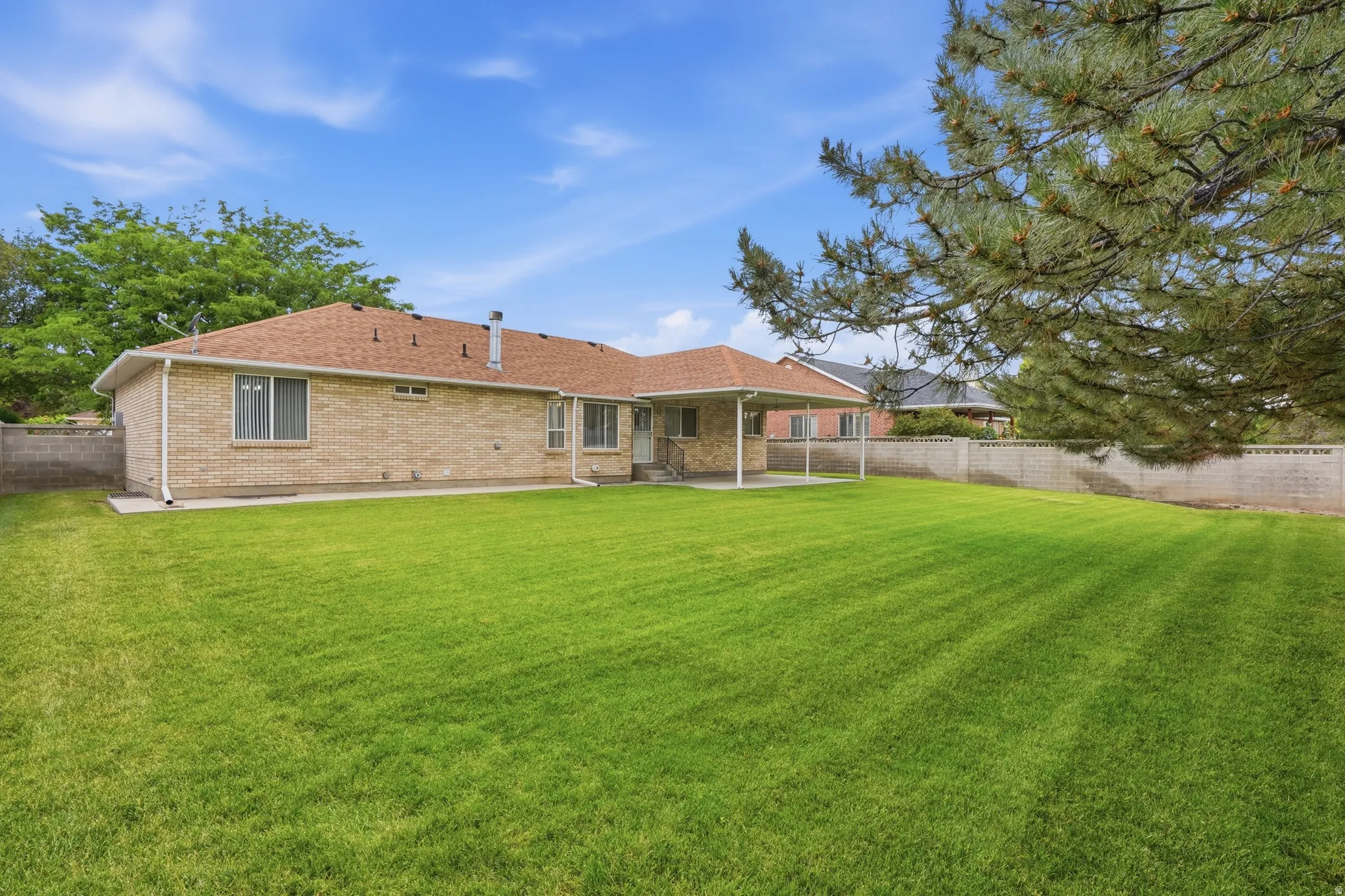 Expansive rear yard featuring a manicured lawn, full brick exterior, a covered patio, and a privacy block wall