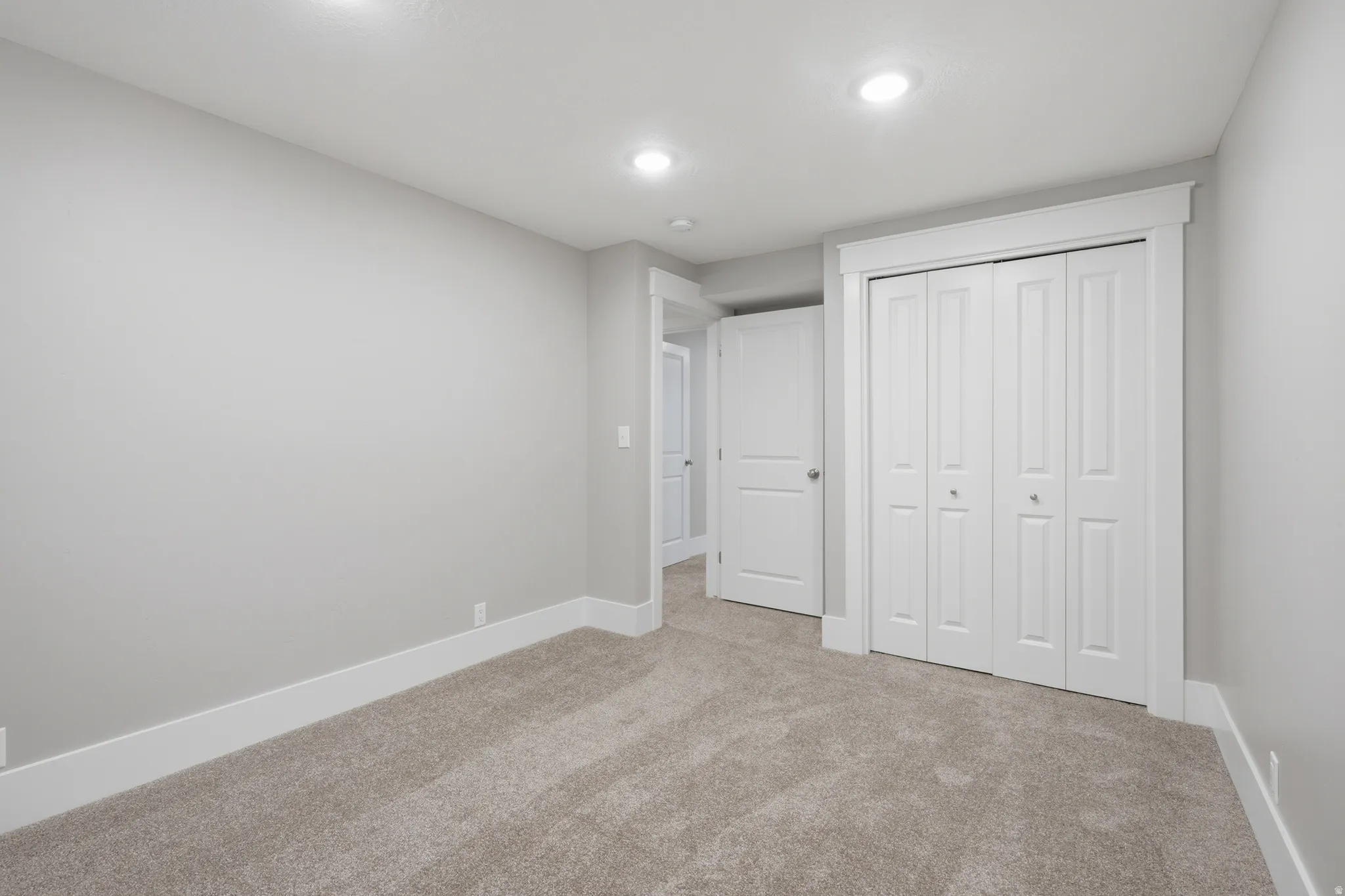 Neutral tone wall color with white trim, recessed lighting, carpet flooring, and bi-fold closet doors