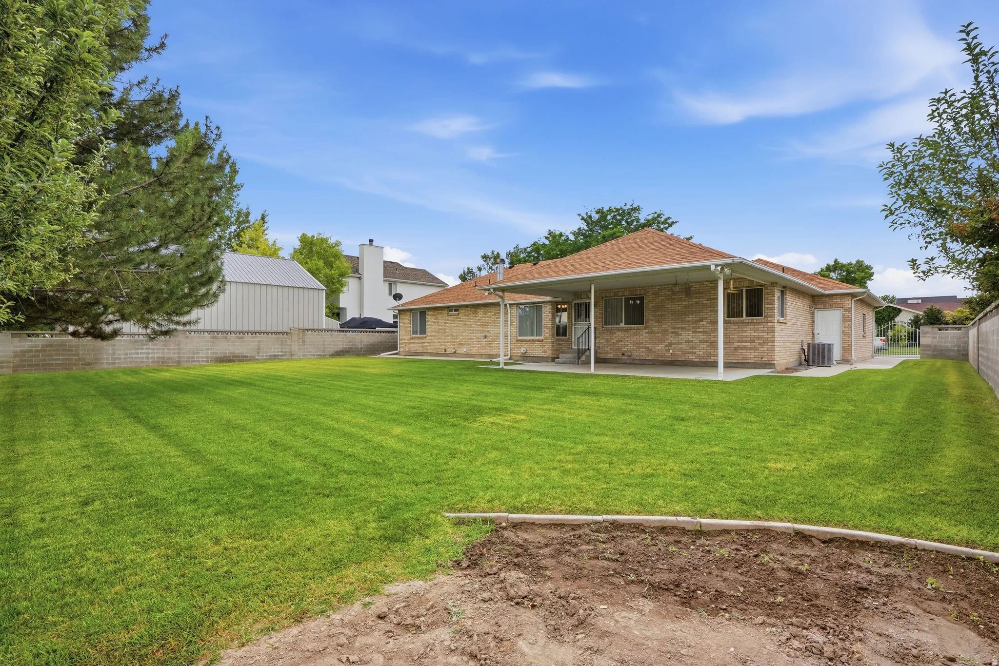 Expansive backyard featuring a manicured lawn, full brick exterior, a covered patio, and mature perimeter trees