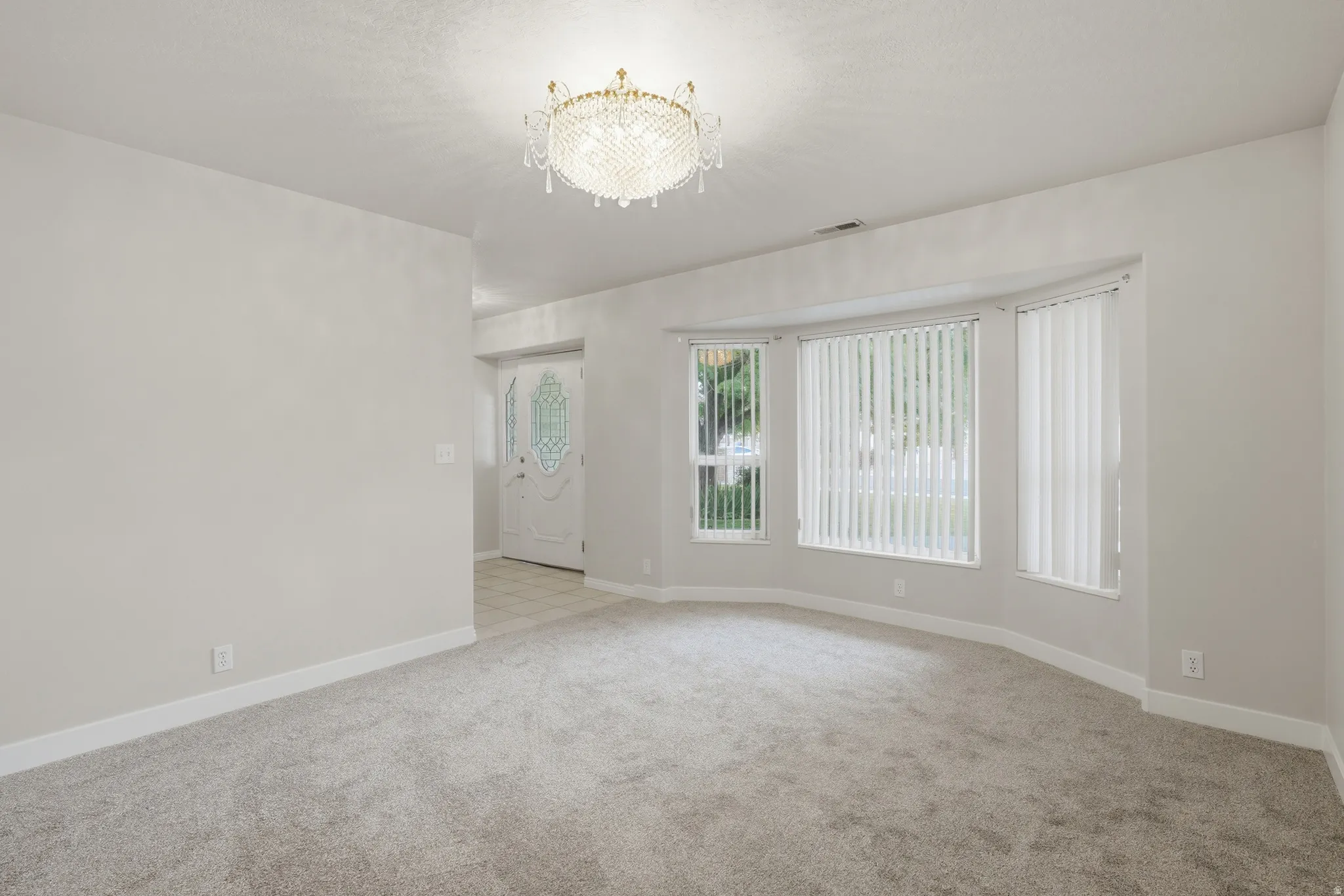 Living area with a bay window, wall-to-wall carpeting, and a crystal chandelier
