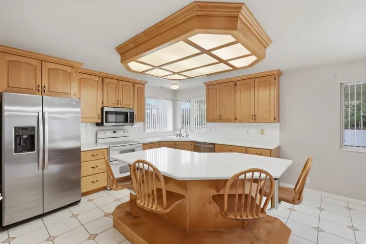 Kitchen with light wood cabinetry, stainless steel appliances, and a built-in island with a white countertop